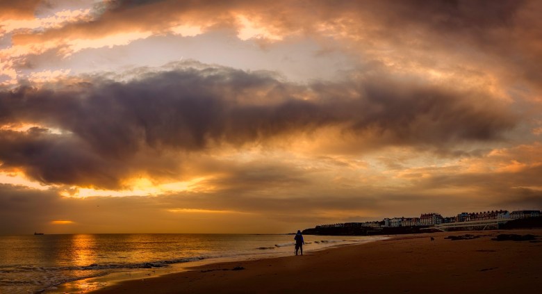 A person walks on a beach after a storm at sunrise as a metaphor for emotional resilience 