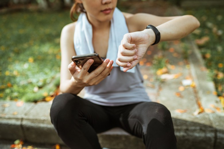 A person checks their fitness tracker after a workout while making an entry in their fitness journal
