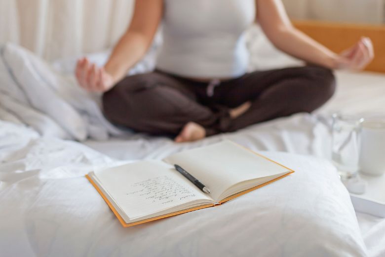 a person meditates with an open notebook for journaling nearby.
