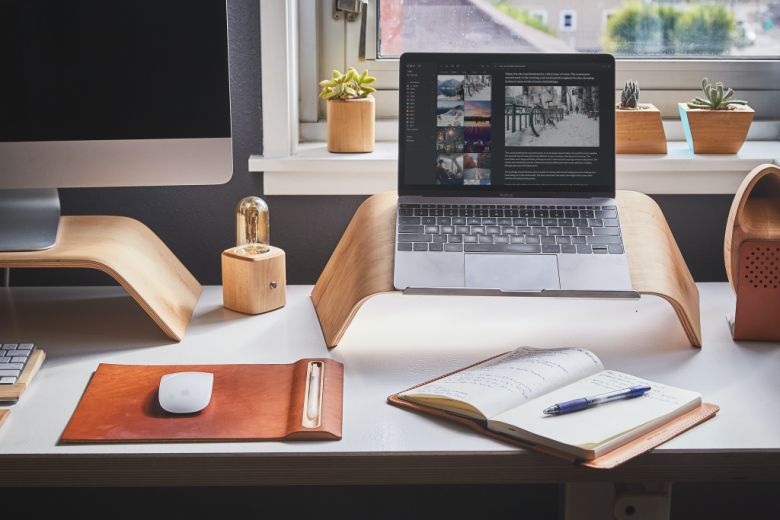A scene of a desk with an open journal notebook and journey entry on a computer