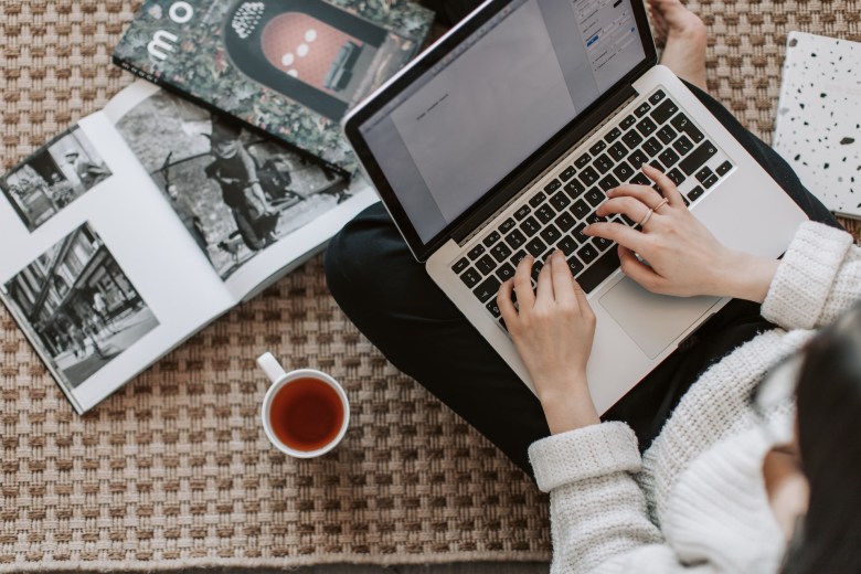 A scene of keeping a journal on a computer next to photo albums with a cup of tea nearby.