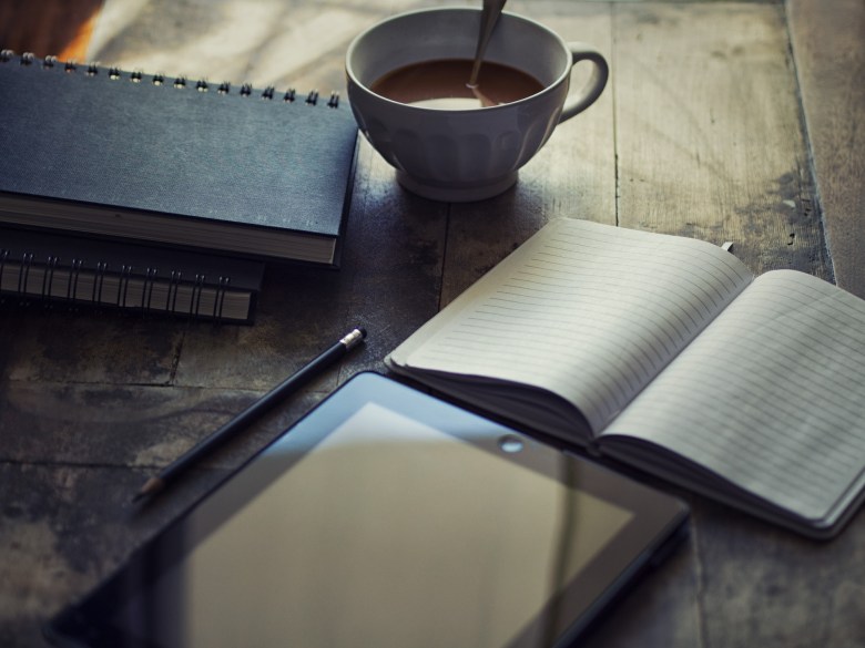 a scene of journaling about feelings with an open notebook, tablet, and a cup of tea.
