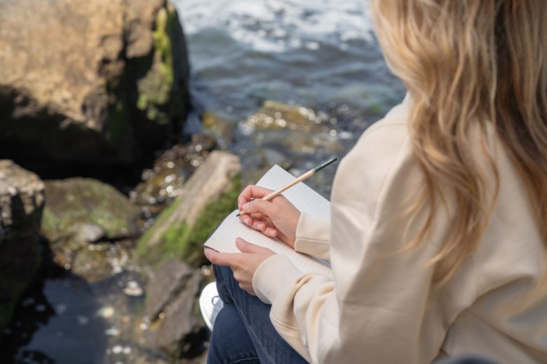 A person writes in a nature journal