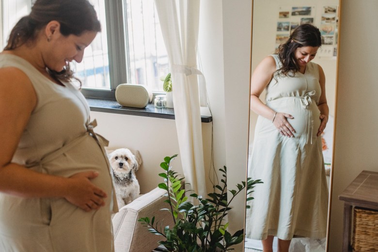 A person looks in the mirror while taking a photo to document in a weekly pregnancy journal